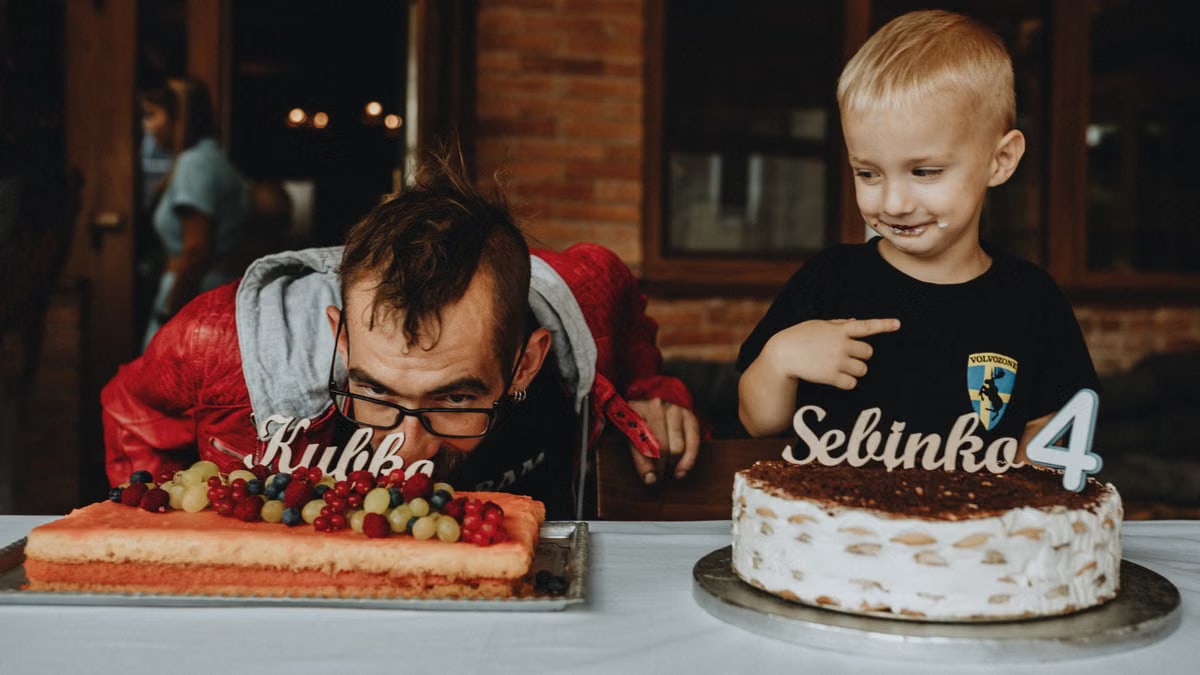 Child and man celebrate birthday with joy, surrounded by cakes and laughter indoors.